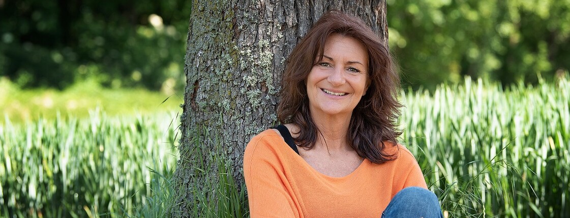 Andra Fuchst sitzt in der Wiese vor einem Baum