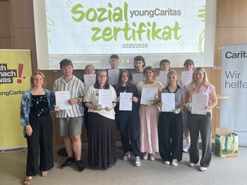 Lehrlinge stehen vor einer Leinwand mit PowerPoint Präsentation der youngCaritas und präsentieren ihre Zertifikate.