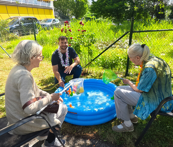 Drei Personen sitzen um ein kleines Plantschbecken.