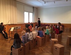Kinder sitzen bei einer musikalischen Präsentation und erleben die Klänge von Geige und Cello in einem Veranstaltungsraum.