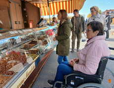 Gruppe von Menschen, einige in Rollstühlen, an einem Marktstand mit Nüssen und Süßigkeiten.