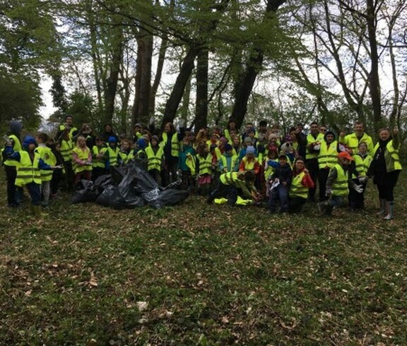 Kinder und Begleitpersonen versammeln sich nach einer Müllsammelaktion im Wald und präsentieren gemeinsam gesammelte Abfälle.