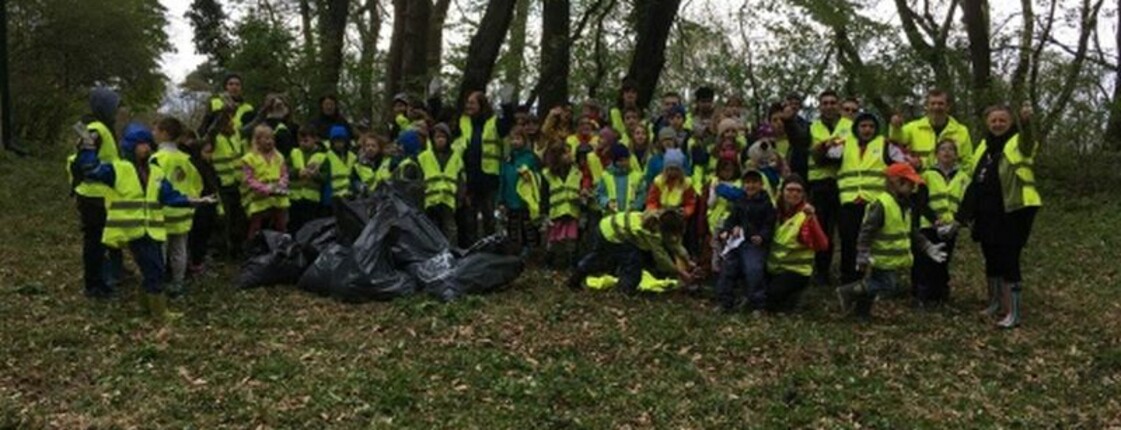 Kinder und Begleitpersonen versammeln sich nach einer Müllsammelaktion im Wald und präsentieren gemeinsam gesammelte Abfälle.
