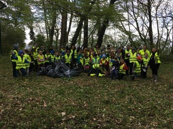 Kinder und Begleitpersonen versammeln sich nach einer Müllsammelaktion im Wald und präsentieren gemeinsam gesammelte Abfälle.