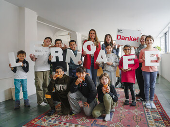 Gruppe von Kindern und zwei Erwachsenen im Lerncafé, hält Buchstaben „LERNCAFE“ und ein „Danke!“-Schild