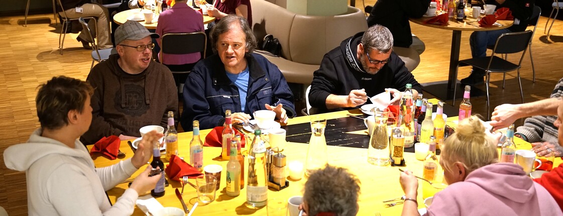 Menschen sitzen an einem Esstisch und unterhalten sich