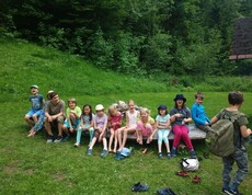 Kinder sitzen während der Projektwoche gemeinsam auf einer Holzbank im Freien und verbringen eine Pause in naturnaher Umgebung.