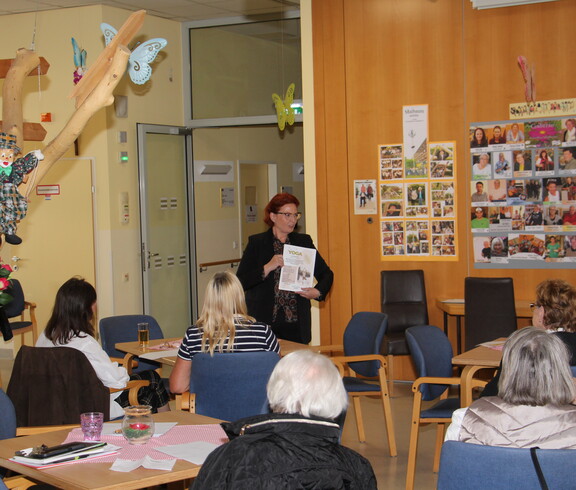 Pflegedienstleiterin Tanja Andraschko steht vor einer Gruppe interessierter Angehöriger und hält eine Rede. Sie wirkt engagiert und spricht mit Blickkontakt ins Publikum.