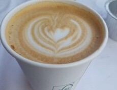 Ein Becher Kaffee mit herzförmigem Milchschaummuster steht auf einem weiß gedeckten Tisch und wurde beim Sommerfest als süße Begleitung zu Waffeln serviert.