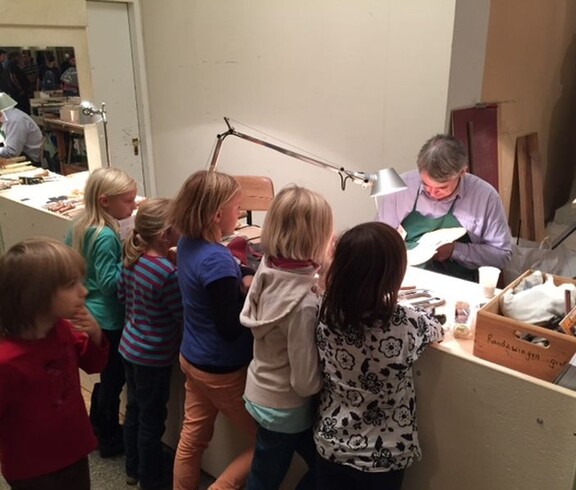 Kinder beobachten in einer Werkstatt die Arbeit eines Geigenbauers und erhalten Einblicke in die Herstellung von Streichinstrumenten.