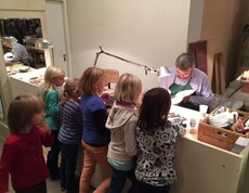 Kinder beobachten in einer Werkstatt die Arbeit eines Geigenbauers und erhalten Einblicke in die Herstellung von Streichinstrumenten.