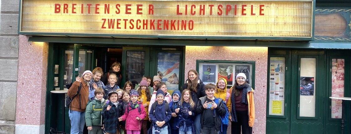 Kinder und Begleitpersonen stehen vor dem Kino Breitenseer Lichtspiele. Der gemeinsame Kinobesuch ist Teil eines schulischen Ausflugs.