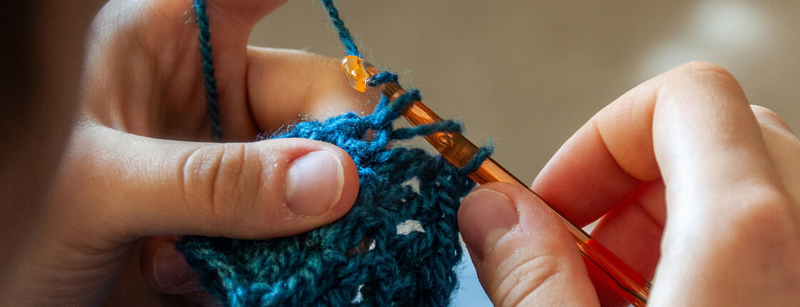 Hände häkeln mit blauer Wolle ein Kleidungsstück für die Aktion gegen Armut in Kärnten.