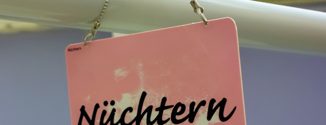 Ein kleines rosa Schild mit der Aufschrift "Nüchtern". Das Schild wurde mit einer dünnen Kette an einer Stange befestigt