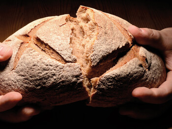 Zwei Hände halten ein großes Brot in der Hand. Es erleuchtet auf schwarzem Hintergrund.