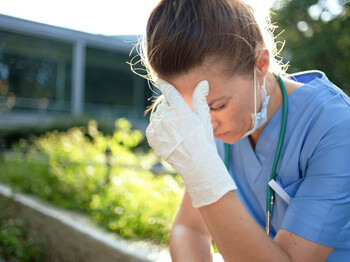 Eine erschöpfte Pflegekraft sitzt auf einem Sessel und stützt den Kopf in die Hände.