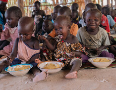 Südsudanesische Kinder sitzen am Boden mit gefüllten Tellern vor sich und essen